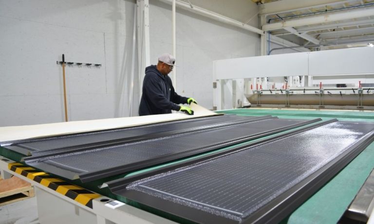 Worker placing a protective sheet over solar roofing panels on a work table.