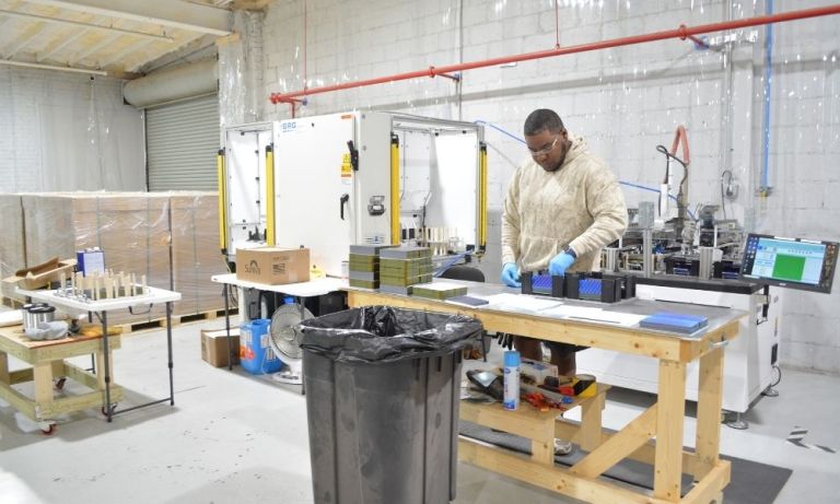 Worker in blue gloves assembling solar parts at a wooden bench.