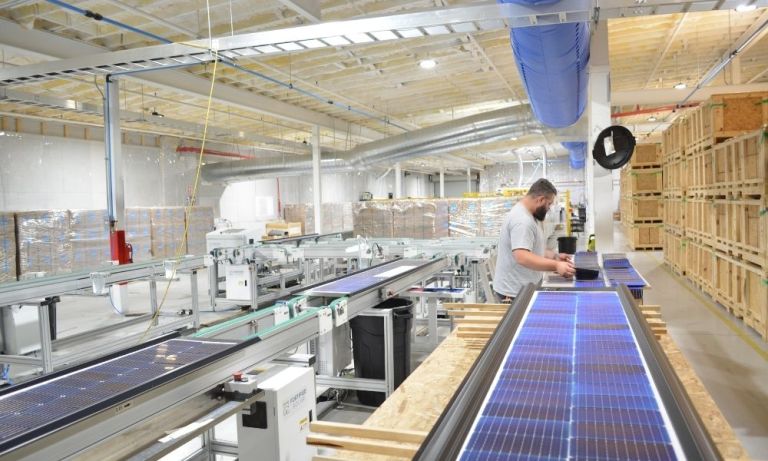 Technician inspecting solar panel strips along a conveyor belt.
